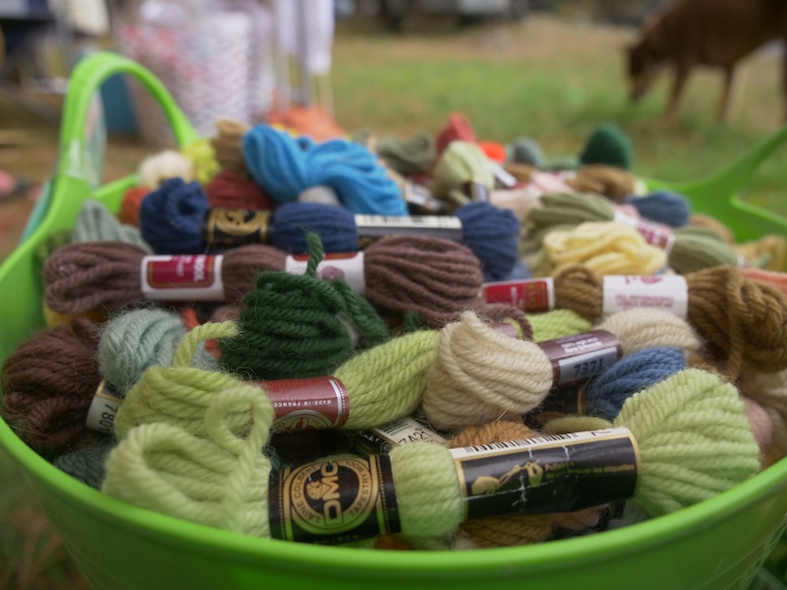 A green plastic tub full of different coloured yarns.