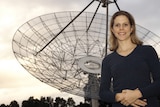 A woman stands in front of an antenna.