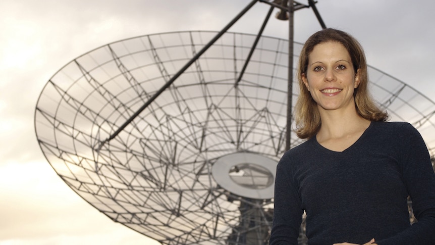 A woman stands in front of an antenna.