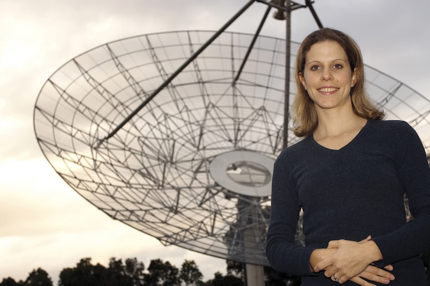 A woman stands in front of an antenna.