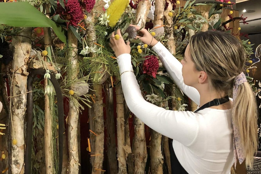 A woman works on an arrangement of native flowers at a florist.