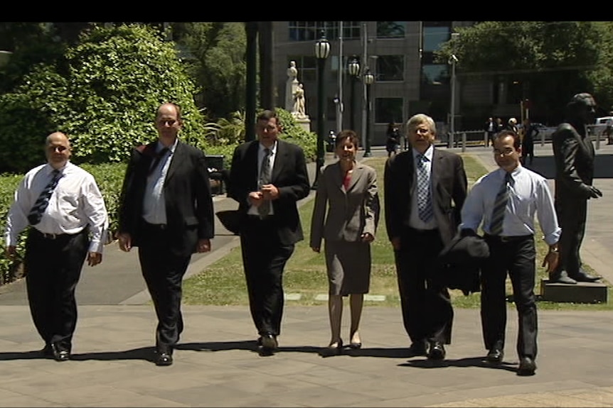 Andrews walks across the paved ground flanked by other members of Labor