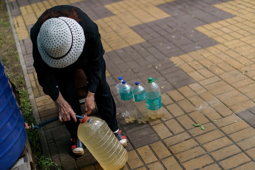 A resident fills up water bottles with brown water in a park near her apartment.