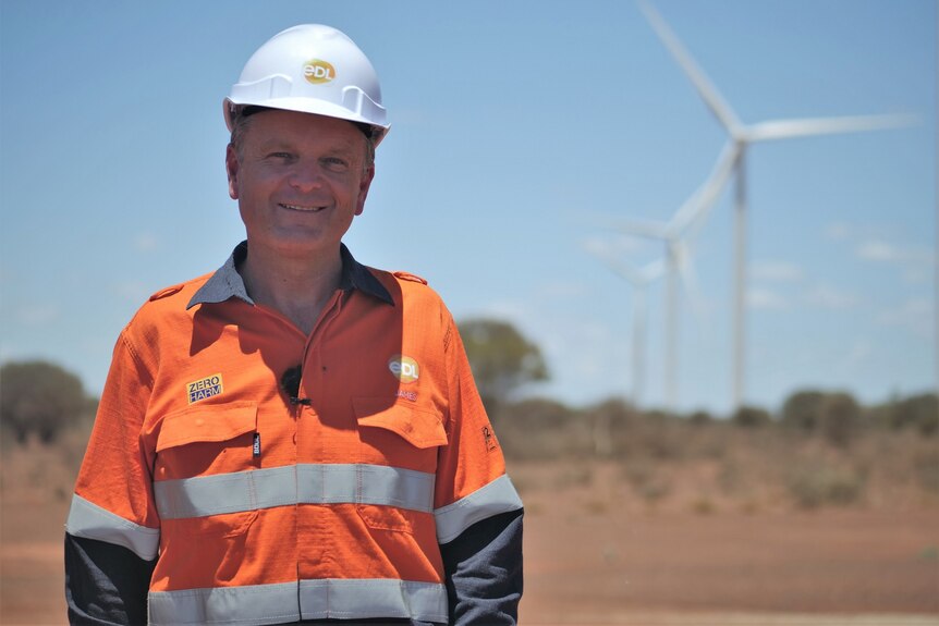 Man wearing hard hat and orange fluoro shirt with wind turbines in background