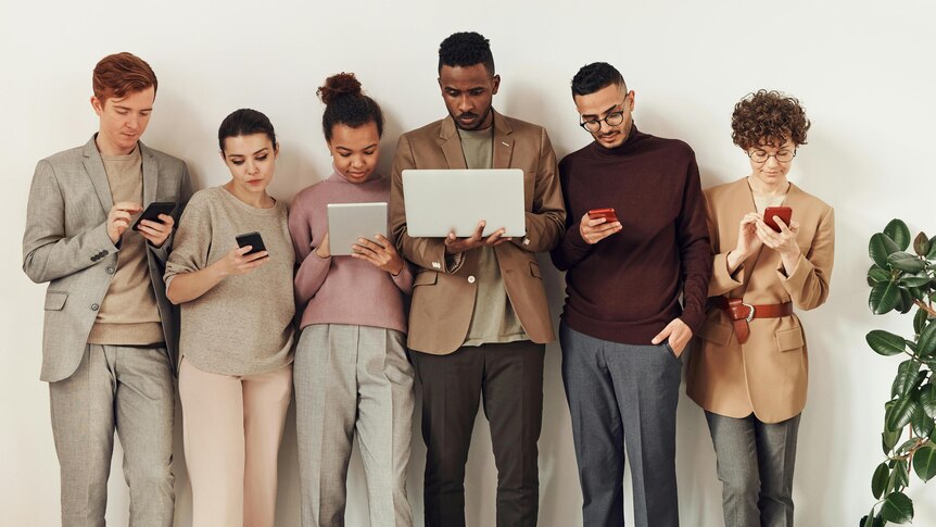 Groups of young people standing against a white wall holding and looking at different devices