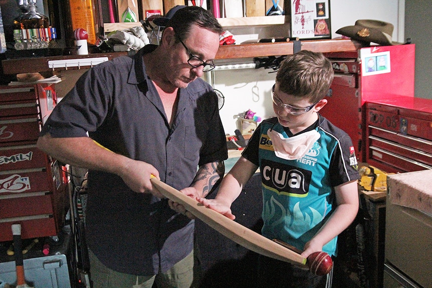 A father with his 10-year-old son inspect a cricket bat in a workshop