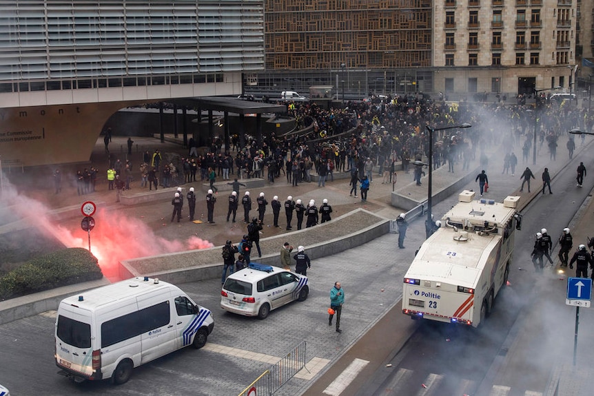 Police stand in front of police vans and trucks as they face a large crowd of protesters