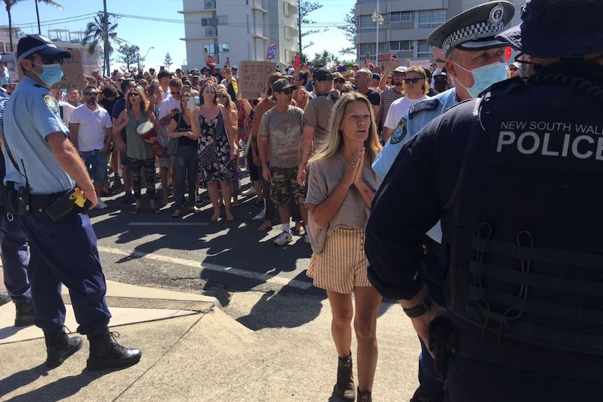 A large crowd of protesters stand facing a line of police on a sunny day in NSW.