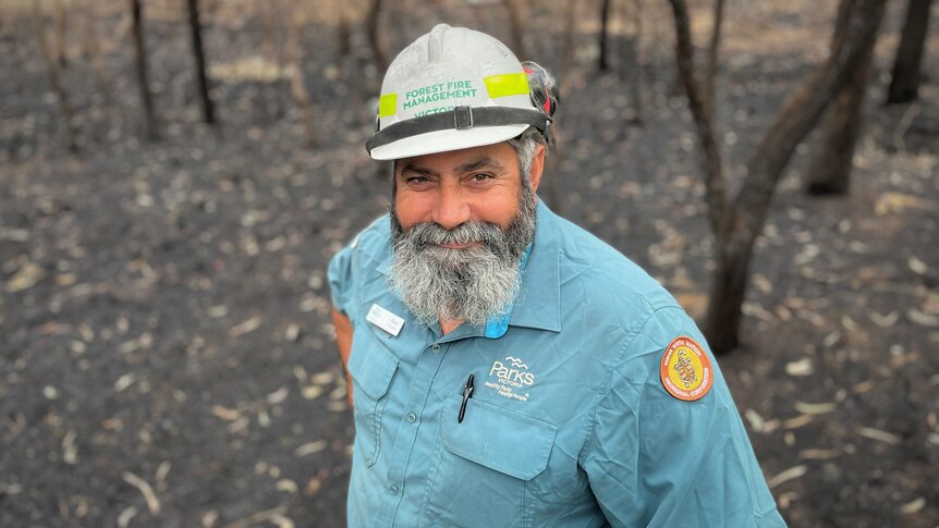 A man stands smiling in front of a bushfire site