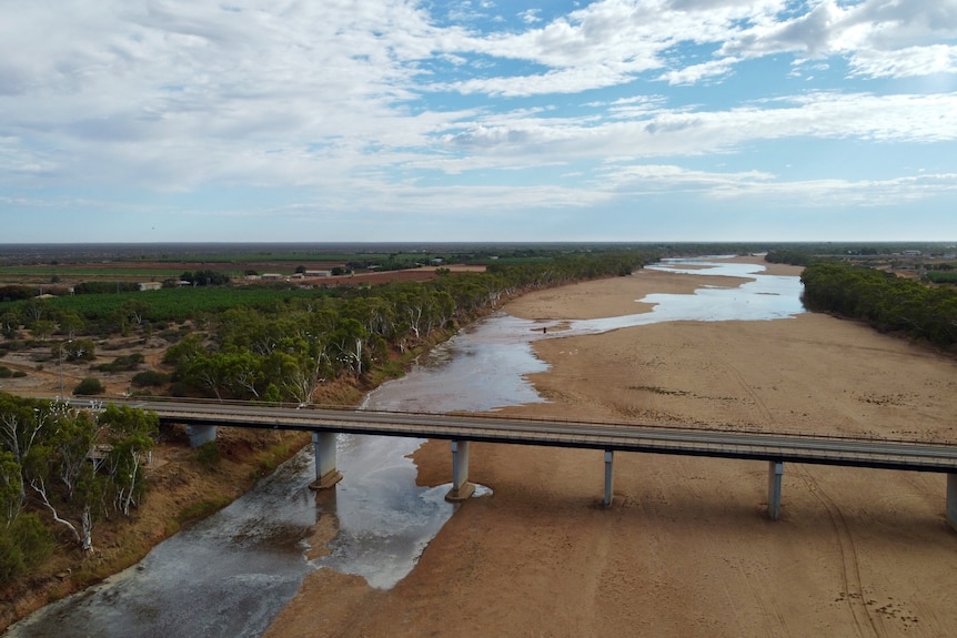 A view of a large sandy river bed from a drone in the sky with river snaking across the vast river bed.