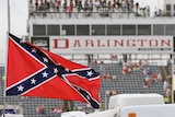 A Confederate flag flutters in the wind, with a motor racing grandstand in the background.