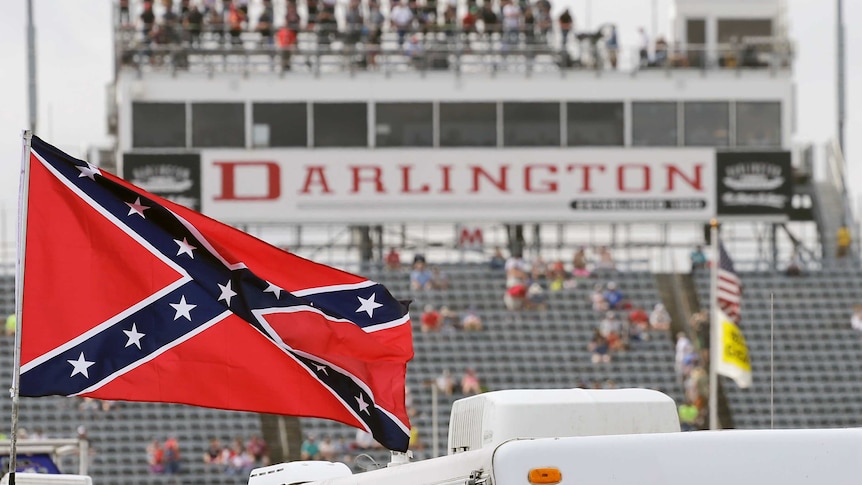 A Confederate flag flutters in the wind, with a motor racing grandstand in the background.