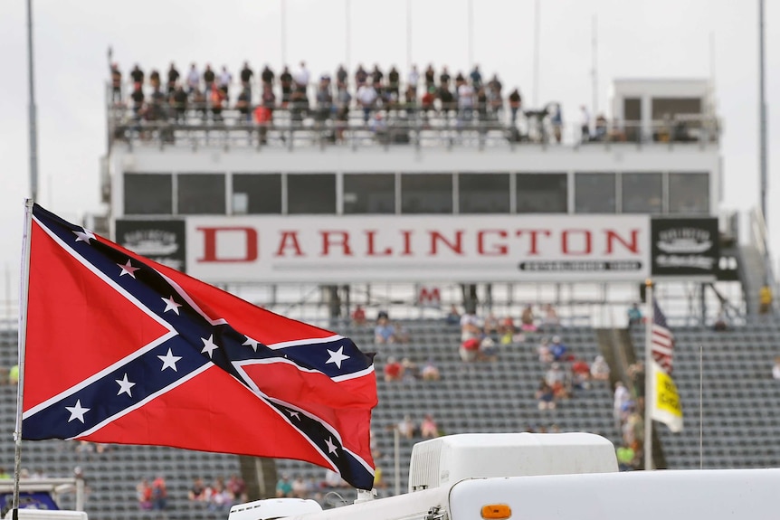 A Confederate flag flutters in the wind, with a motor racing grandstand in the background.