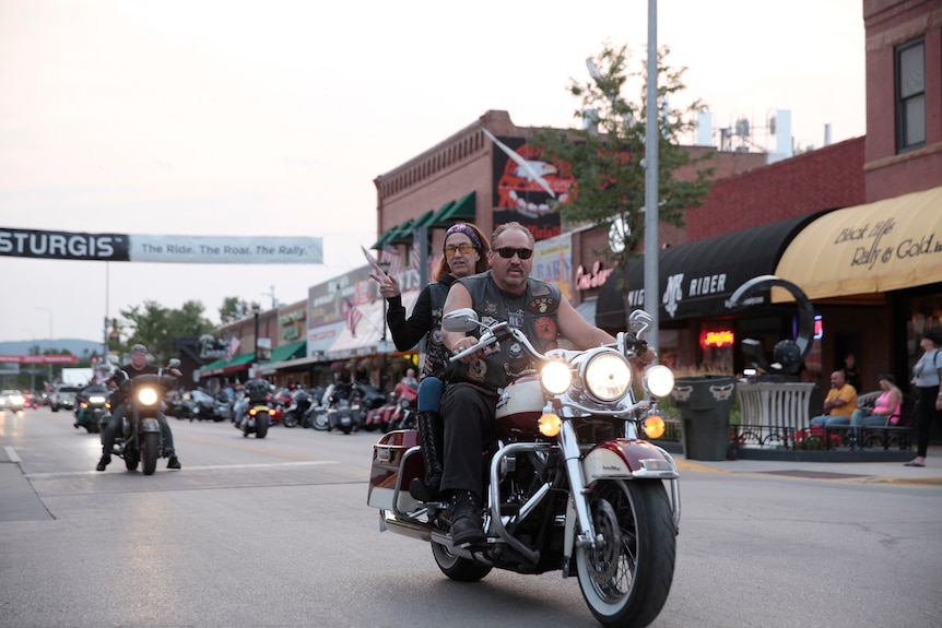 A man and a woman on a motorcycle ride down the main street of a town.