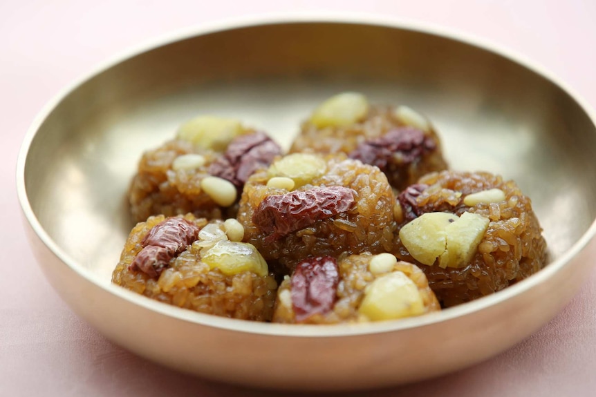 Mounds of sticky rice topped with nuts and dried fruit in a bowl.