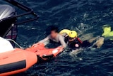 A man being held by a rescue worker lifted on to a boat