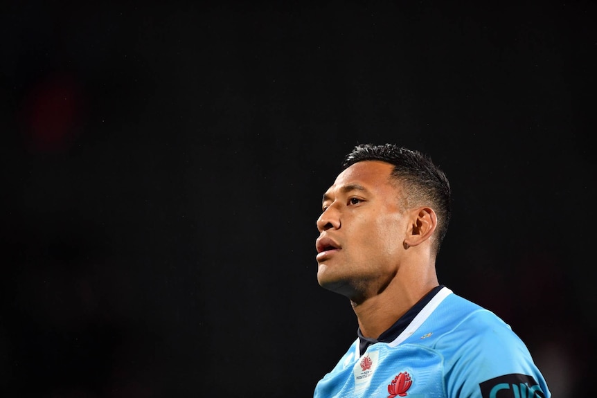 Israel Folau looks off to one side wearing a blue rugby jersey with a black background