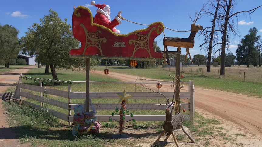 Red santa sleigh and reindeer hoisted in the air with wooden reindeer and presents below 