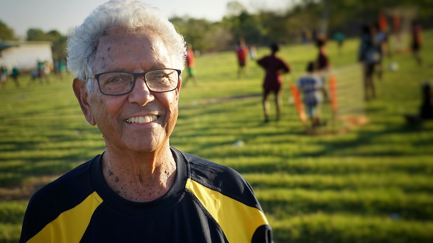 John Moriarty wears a soccer shirt and smiles at the camera, while standing on a field