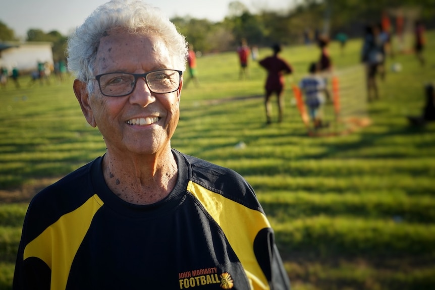 John Moriarty wears a soccer shirt and smiles at the camera, while standing on a field