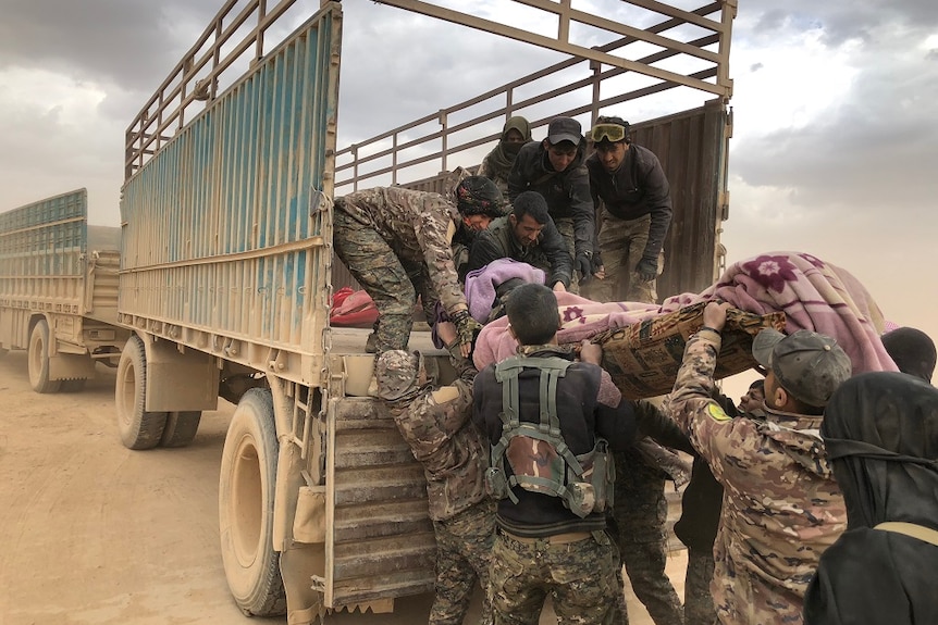 A woman on a stretcher who is wrapped in blankets is lifted into the back of a truck by a group of people in military fatigues.