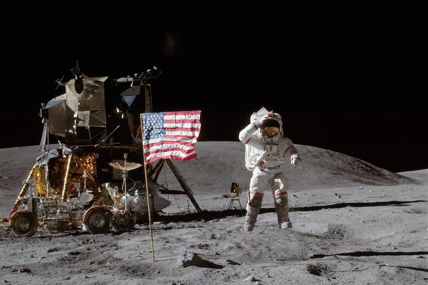 Astronaut salutes to camera standing by American flag on the moon. 
