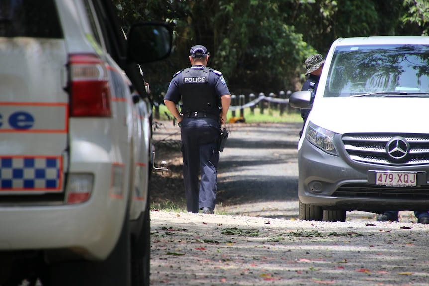 A police man walks towards a park next near two police cars