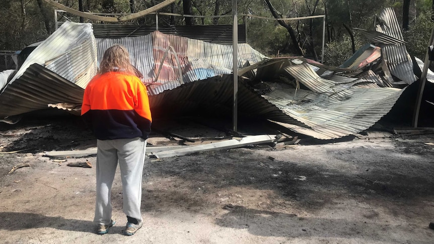 A woman looks at a burnt shed, with a collapsed roof