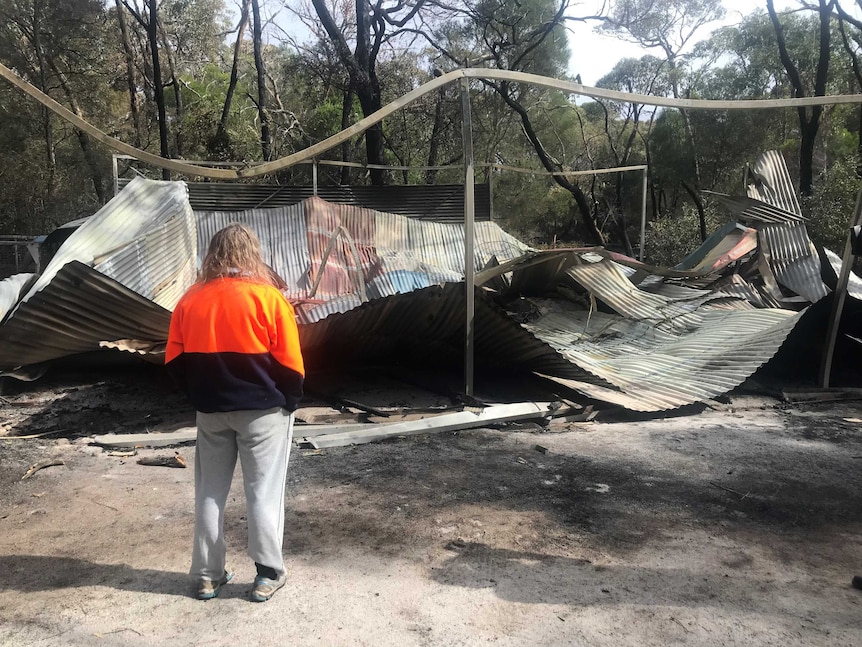 A woman looks at a burnt shed, with a collapsed roof