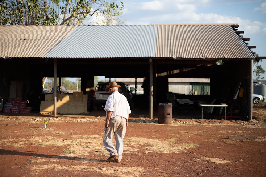 90-year-old former stockmen Bill Harney walks on red dirt past an old tin shed