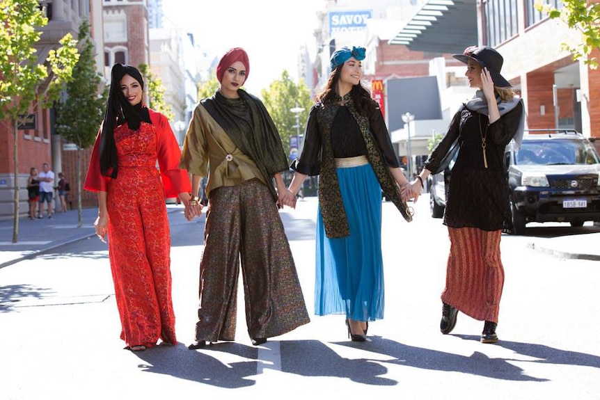 Four modest fashion models stand in the street holding hands.
