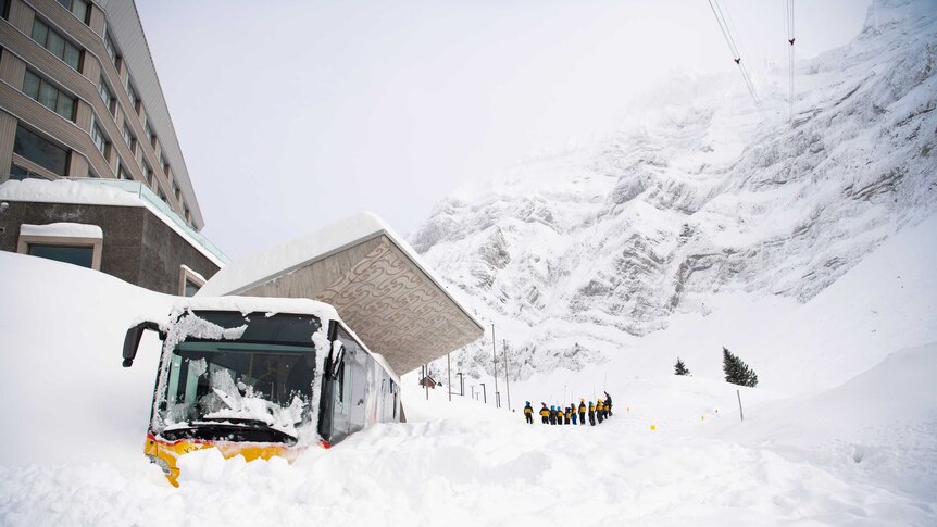 Snow piled up outside a hotel entrance where a bus is also completely covered over in snow