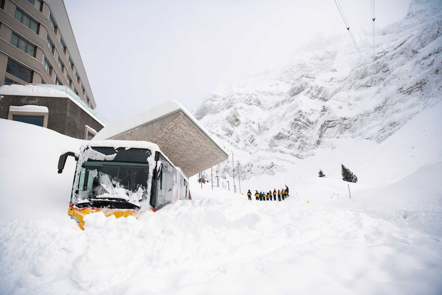 Snow piled up outside a hotel entrance where a bus is also completely covered over in snow