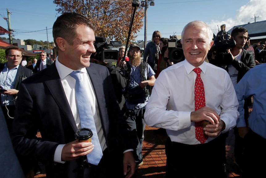 Mike Baird and Malcolm Turnbull walk down a street in Merimbula surrounded by media.