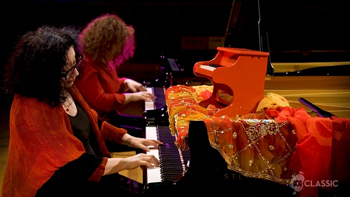 Elena Kats-Chernin and Tamara-Anna Cislowska play at two grand pianos. A toy piano sits on the front piano.
