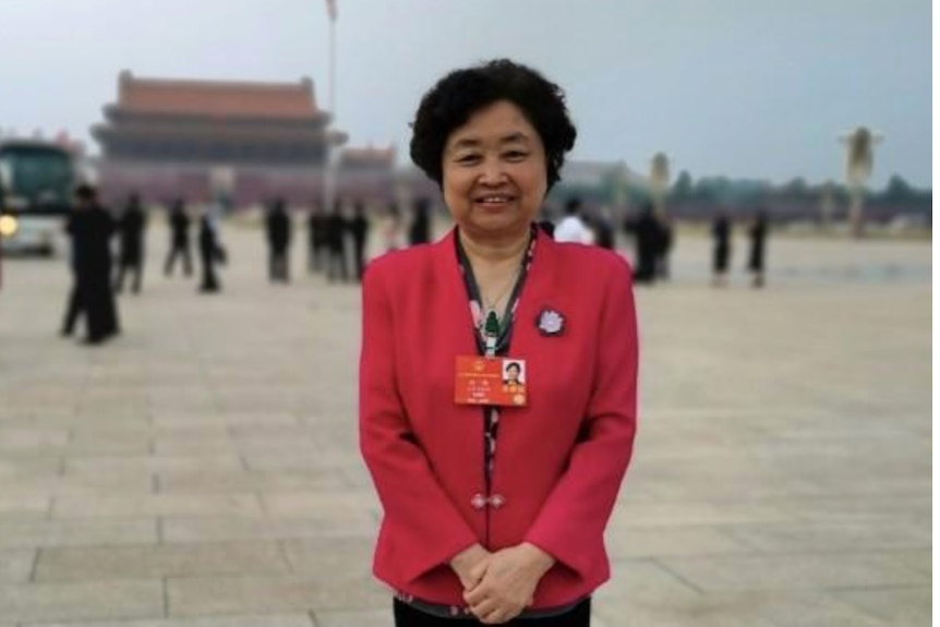 A woman in a red jacket with an identity card around her neck stands in Tiananmen Square in Beijing