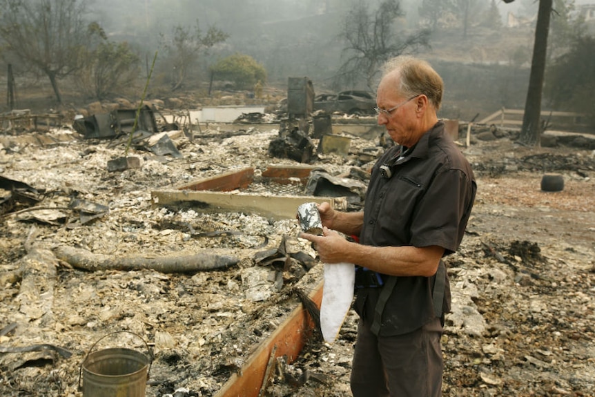 Chuck Rippey looks over a cup found in the burned out remains of his parents' home