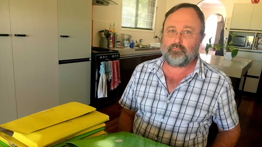 A man sits at his kitchen table with folders of legal documents in front of him.