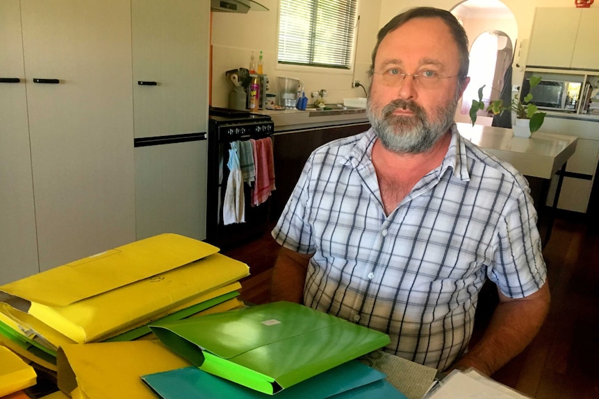 A man sits at his kitchen table with folders of legal documents in front of him.