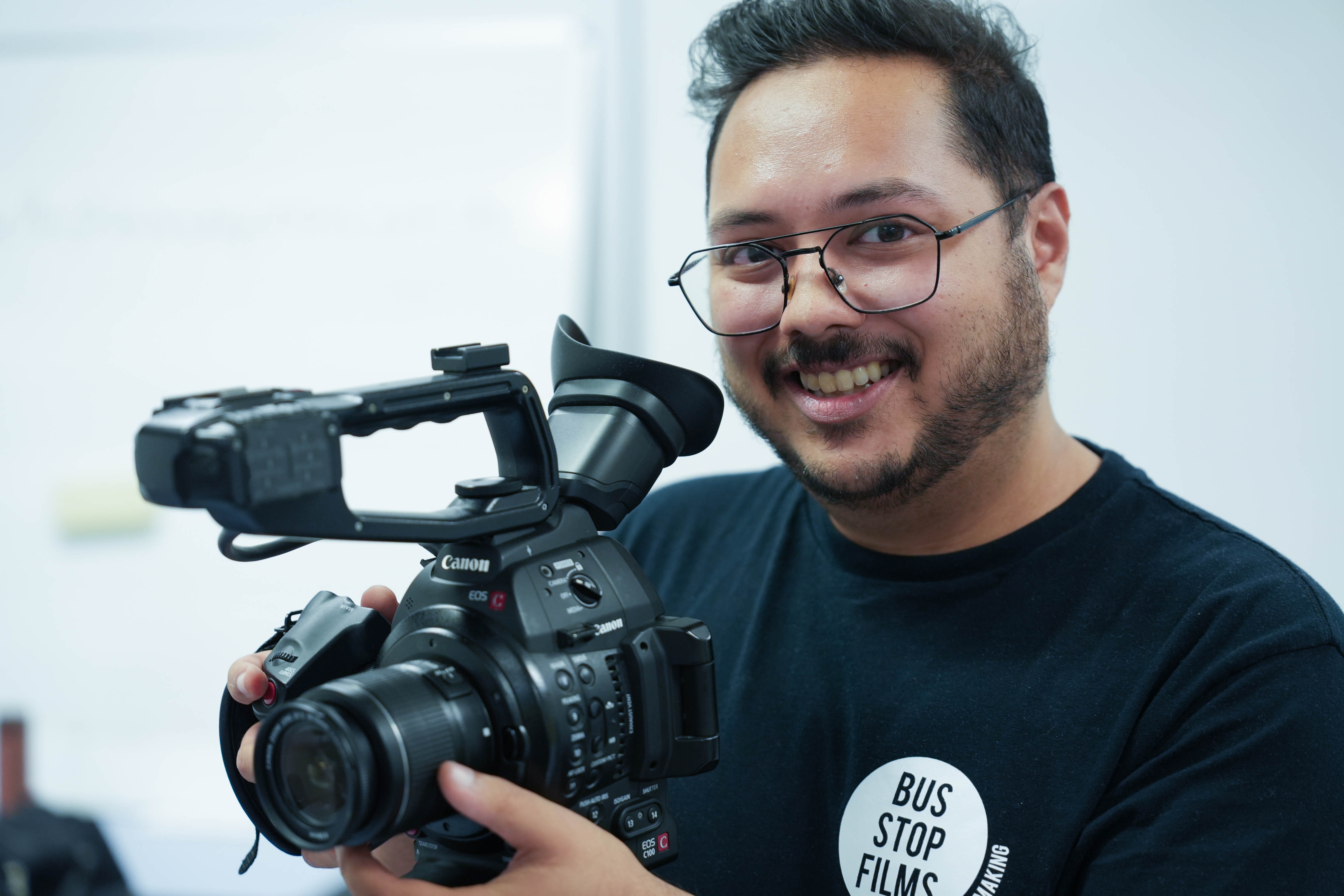 Uma foto de um homem de óculos e camiseta preta segurando uma câmera
