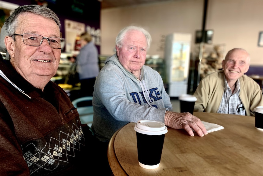 Three older men sit at a table in a cafe