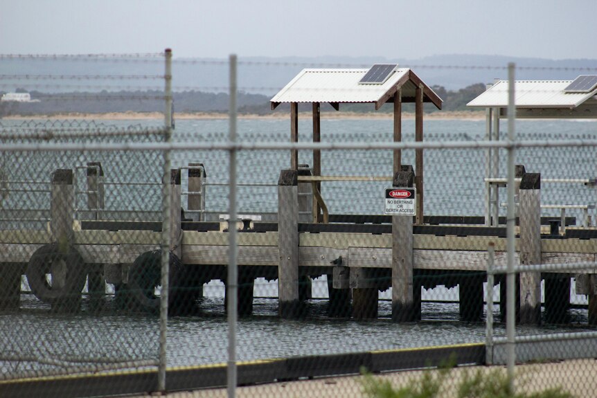 A jetty behind barbed wire fence with a warning sign on it