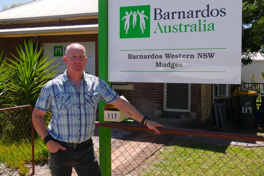 A bald man standing in front of a sign reading Barnardos