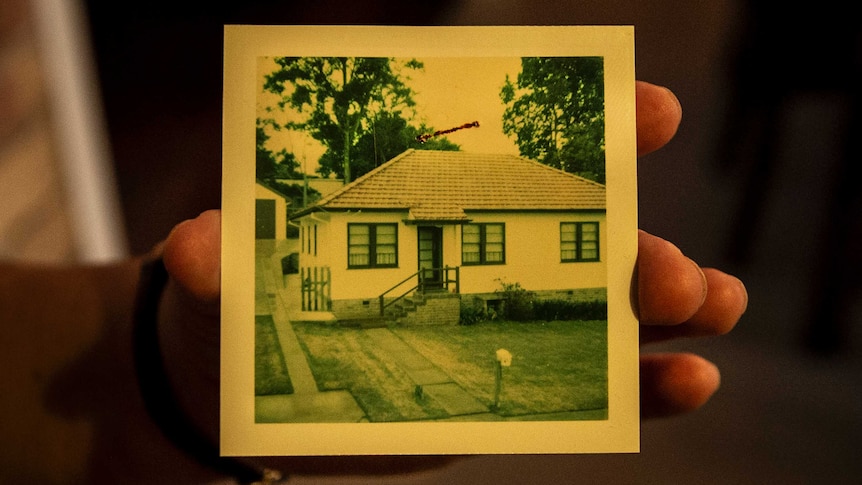 A hand holding an old photo of a house.
