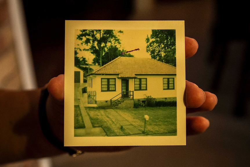 A hand holding an old photo of a house.