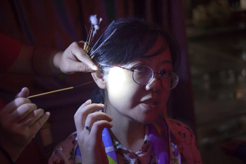 A woman sits as someone sticks a thin wire into her ear.