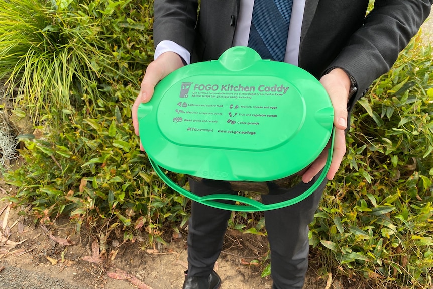 A person wearing a suit holds a green topped bin.
