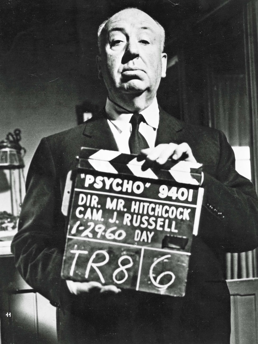 Black and white photo of Alfred Hitchcock holding a clapper board from Psycho.