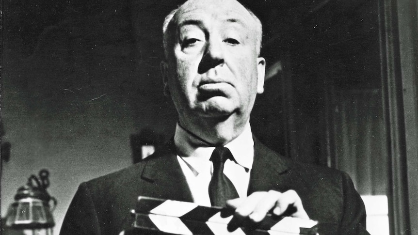 Black and white photo of Alfred Hitchcock holding a clapper board from Psycho.