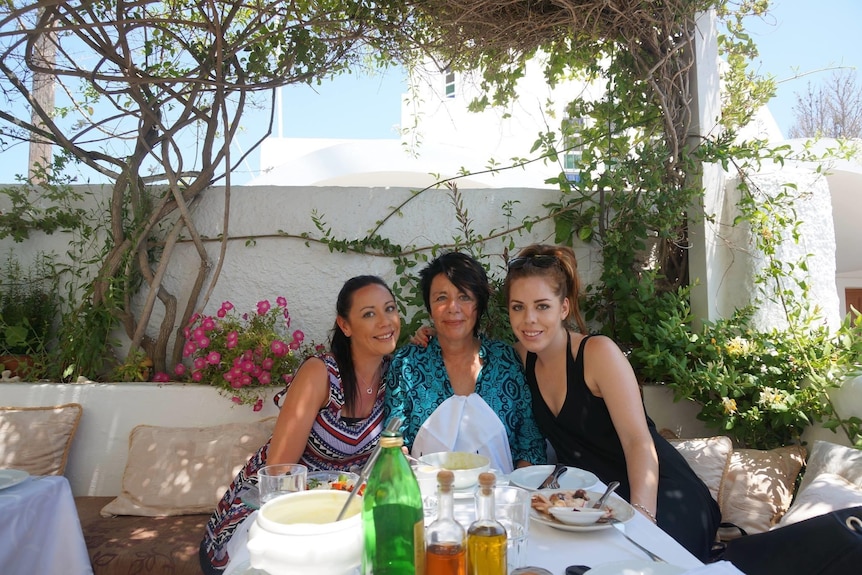 A woman sits at a breakfast tabler with her two adult daughters.